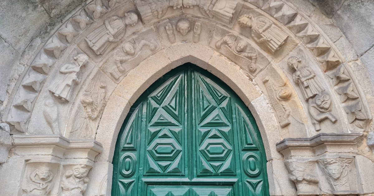 Arco de piedra con tallas antiguas que enmarca una puerta de madera, como las puertas de los templos que recibe el peregrino