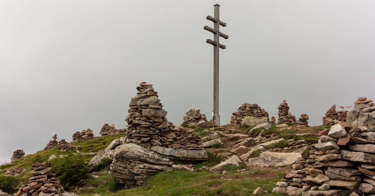 Cruz sobre un montículo de piedras en lo alto de un monte en un día nublado, escena parecida a la Cruz de Ferro