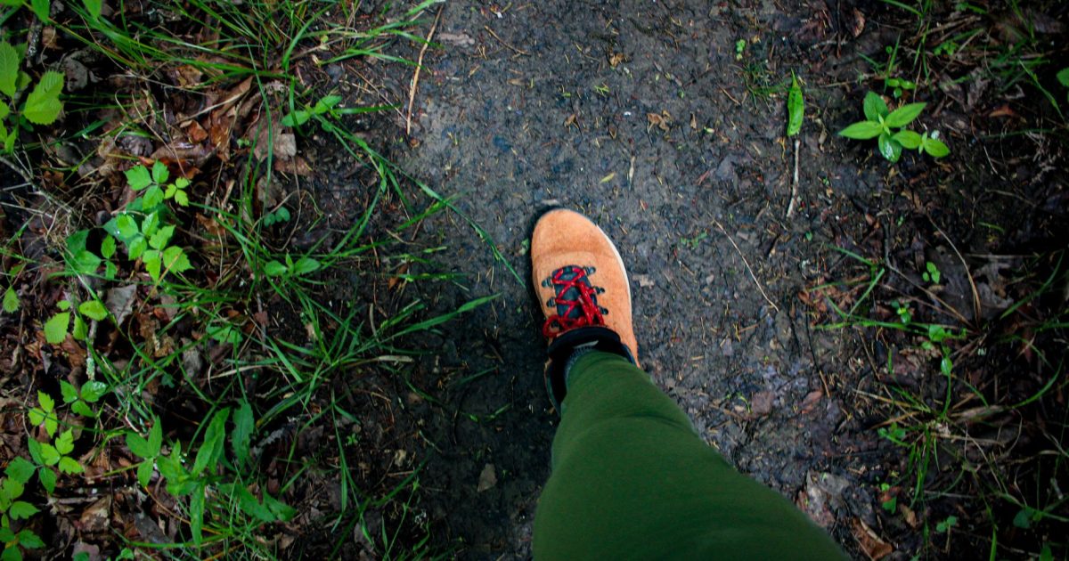 Primer plano de una bota de montaña pisando un sendero de tierra rodeado de vegetación verde