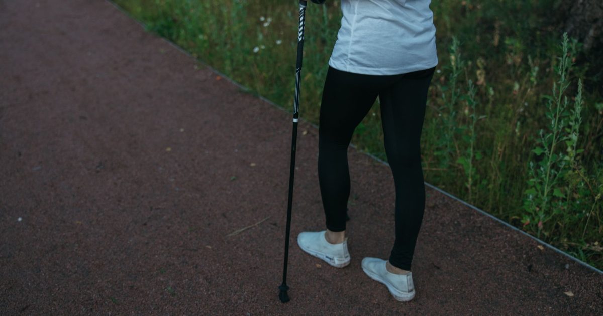 Persona con ropa deportiva caminando con un bastón de senderismo por un camino de tierra en el bosque